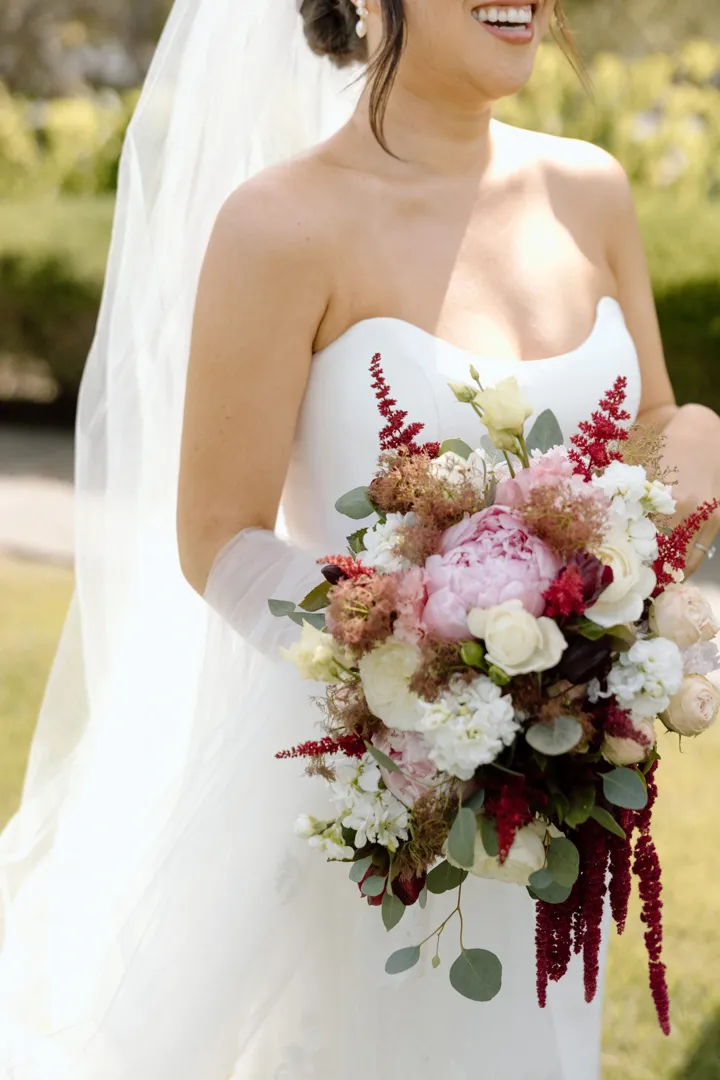 Bride holding a bouquet of pink peonies, white roses and red amaranth