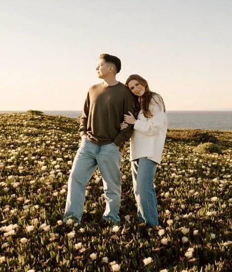 Engaged couple embracing in a field of wildflowers above the ocean
